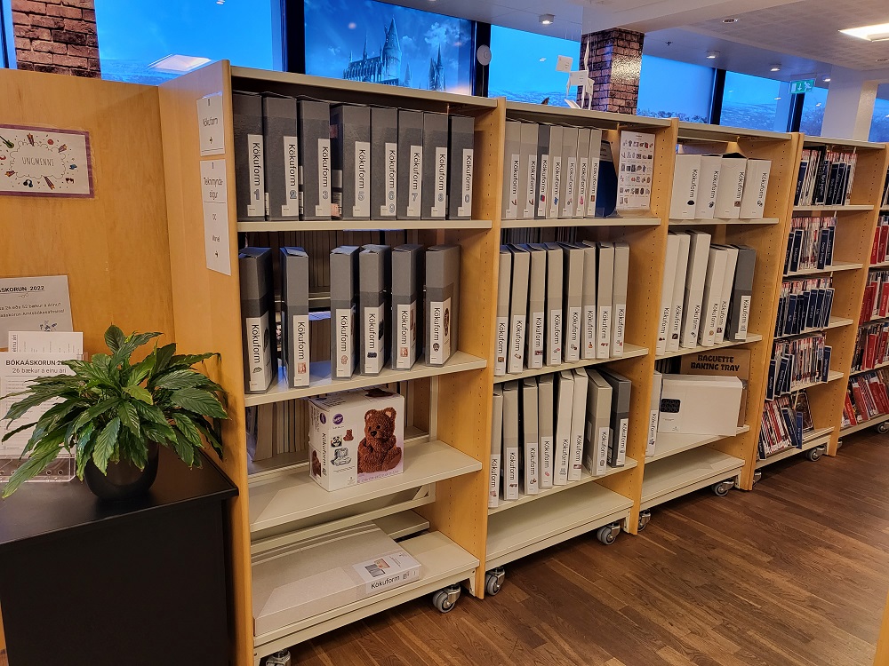 Mynd af bökunarformum í kössum í bókahillum