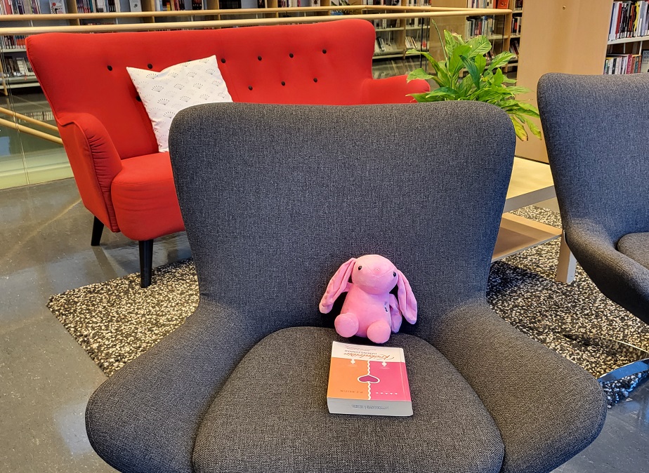 Mynd af bleikri tuskukanínu í stól og bók fyrir framan hana