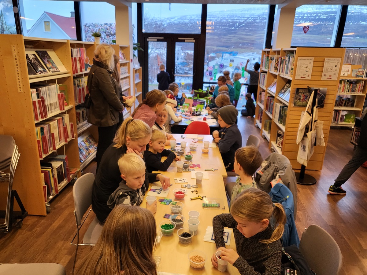 Börn og foreldrar sitja við borð að gera pappa-föndur og mósaík perlur