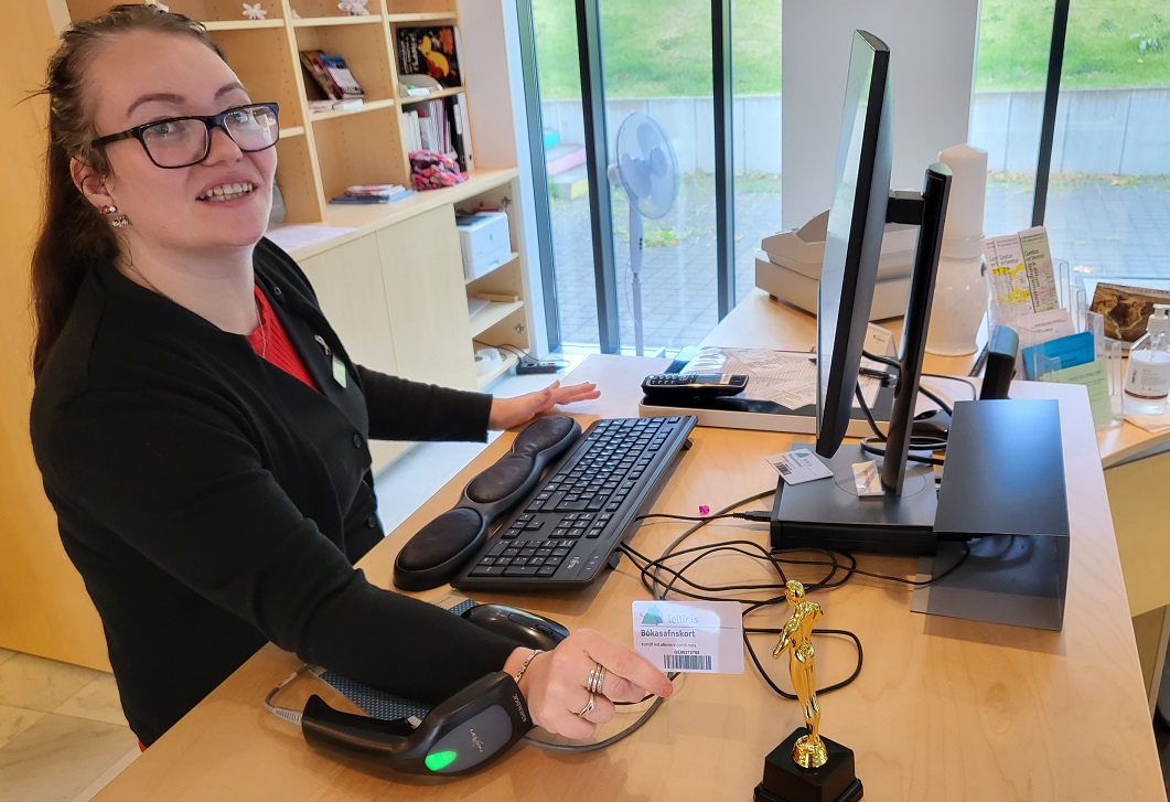 Óskarsstytta á afgreiðsluborði á bókasafni og starfsmaður stendur við